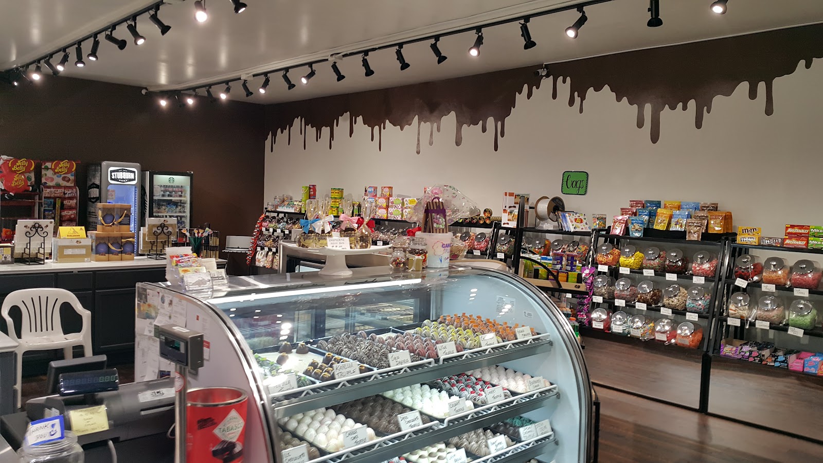 Wide in-store view with curved chocolate display case and chocolate-drip wall